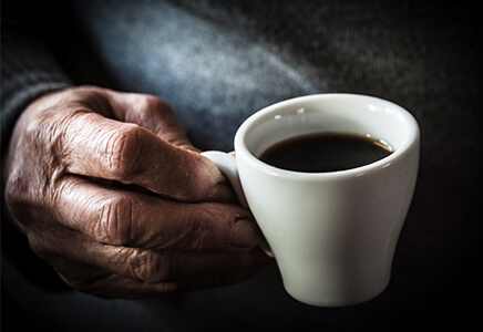 Older hand holding cup of coffee